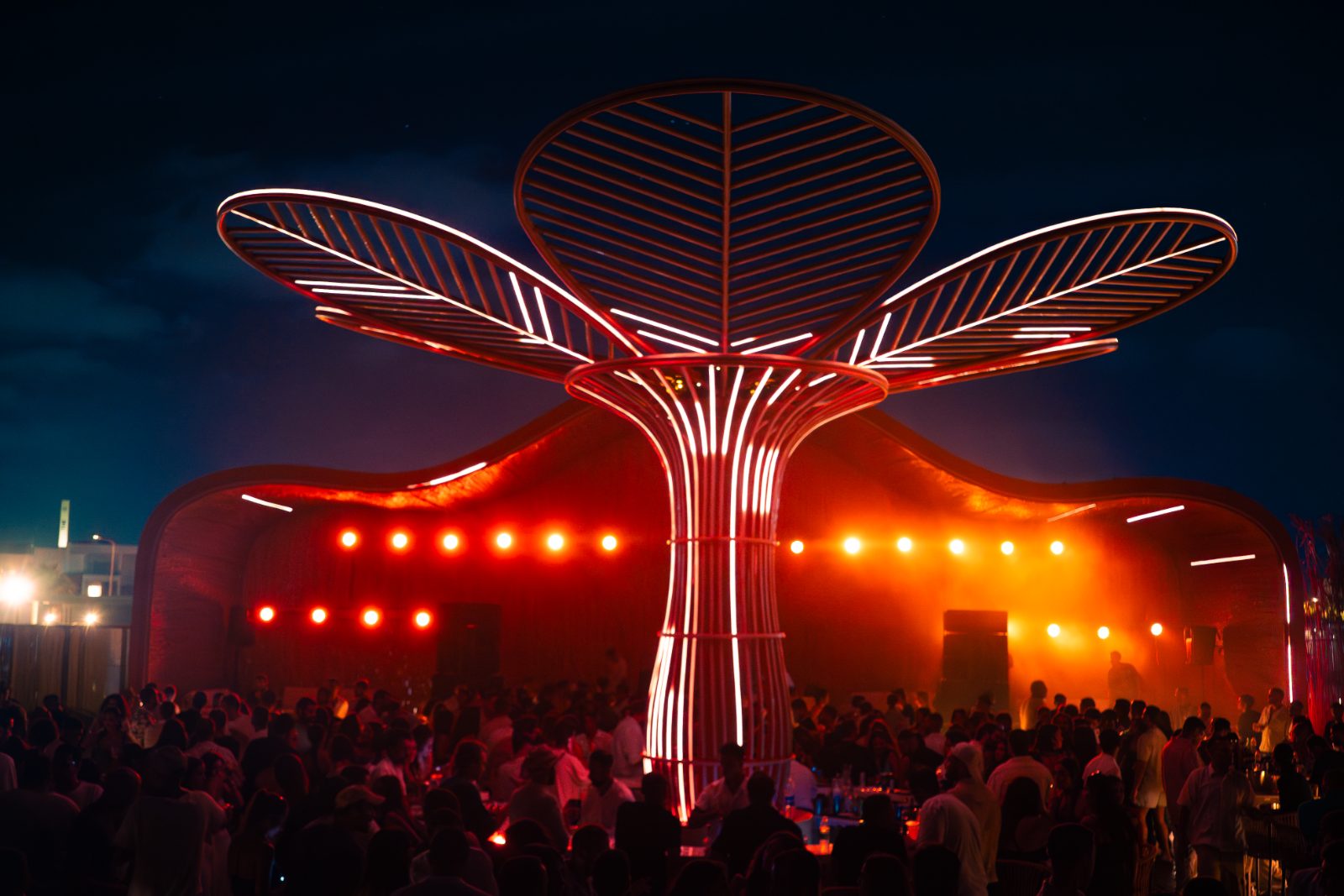 Illuminated flower-petal pavilion above a crowd at a Casa Très event
