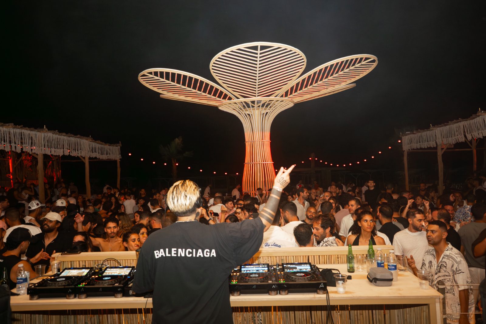 DJ headlining in front of a white petal sculpture before a large crowd at a Casa Très event
