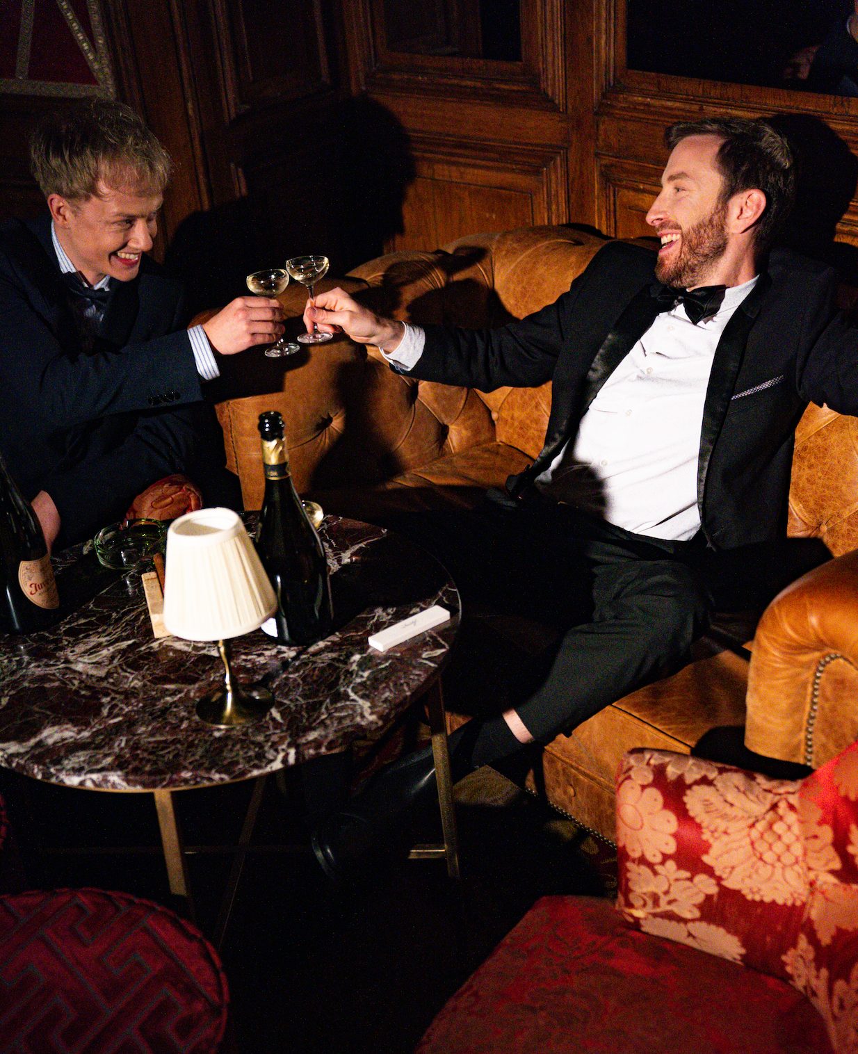Two men in tuxedos and bow ties toasting champagne at a Casa Très black-tie event